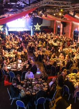 An event hall filled with people at tables and a stage in the distance.