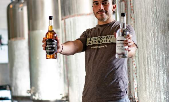 Photo of Alex Voss of Alligator Bay Distillers holding two rum bottles in front of fermentation tank