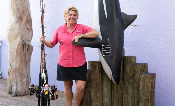 Brenda Hillberry of King Fisher Fleet posing with rods and plaster hanging shark at Fishermen's Village in Punta Gorda