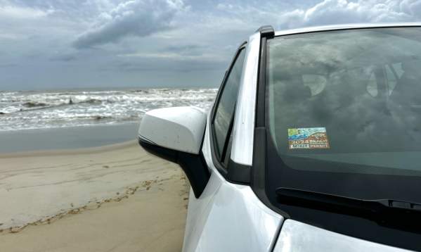 White car on the beach with a parking pass on the window for 2024