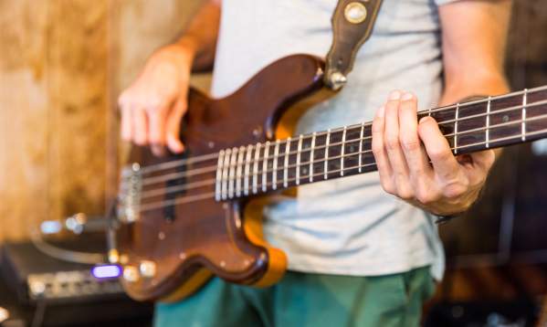 A close up of a guy strumming a brown guitar.
