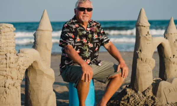 Mark Landrum sits on the beach between two sandcastles under construction in Port Aransas, TX