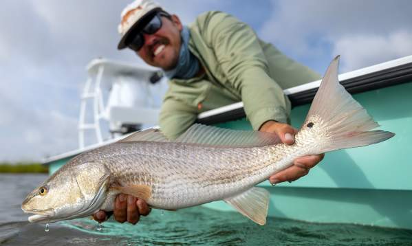 A man in a green shirt and white cap smiling while holding a large redfish (Red drum) on a boat in Port Aransas.
