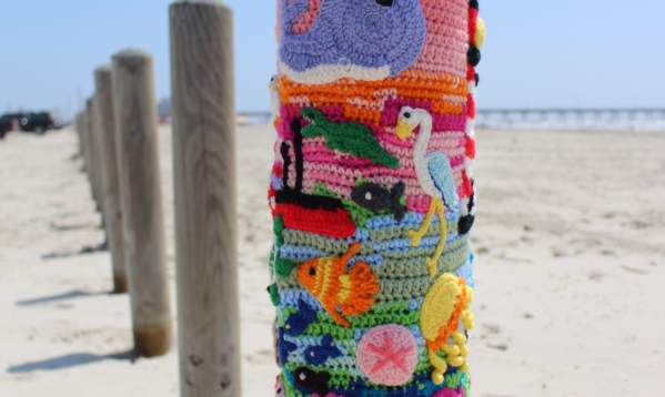 A colorful ballard buddy with all diffrent sea creatues on it. It is an a wooden bollard on the beach.