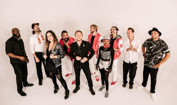 Nine-person band posing in front of a plain background