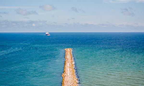 Rock jetty sticking out into the blue and green ocean on a sunny day.