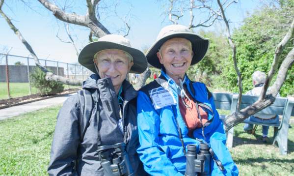 Two women wearing hats and binoculars smile for the camera.