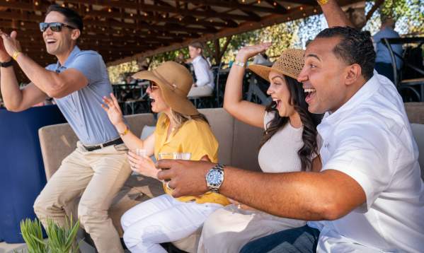 Two men and woman couples cheering while sitting outside on a couch watching a competition.