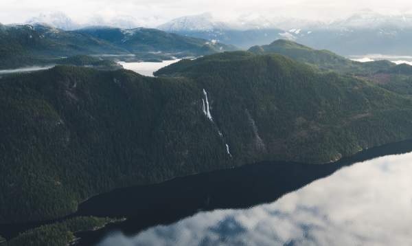 An aerial view of a coastal waterfall, mountains, and the ocean.