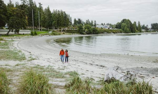 A couple walk down the beach, holding hands.