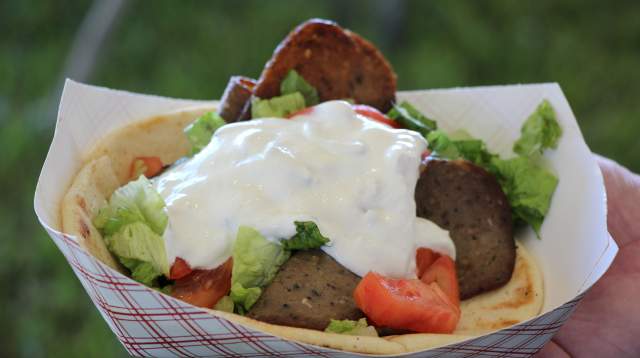 A close-up of a freshly made gyro in a paper tray, topped with tzatziki sauce, lettuce, tomato, and sliced meat on warm pita bread in Fayetteville, NC.