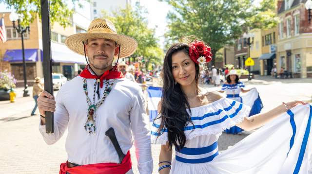 Couple dressed in traditional Central American attire posing during the International Folk Festival parade in downtown Fayetteville, NC, surrounded by music, culture, and color.