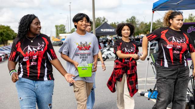 Teens and tweens walk together in matching marching band shirts at an outdoor event in Cumberland County, NC, smiling and chatting in the sunshine.