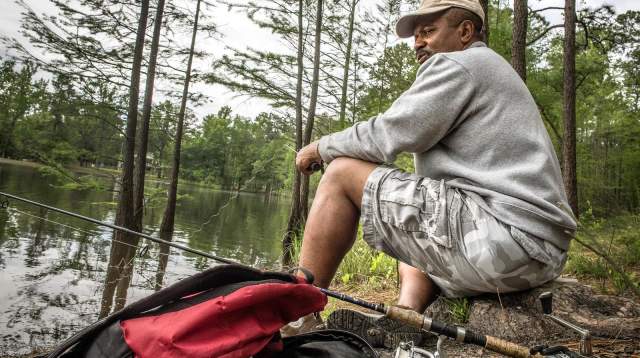 Man fishing along the shoreline at Carvers Creek State Park, surrounded by pine trees and calm water.