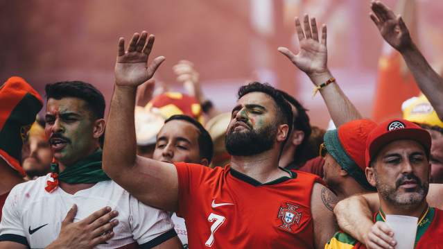Men wearing red and white jerseys watching intense soccer game.