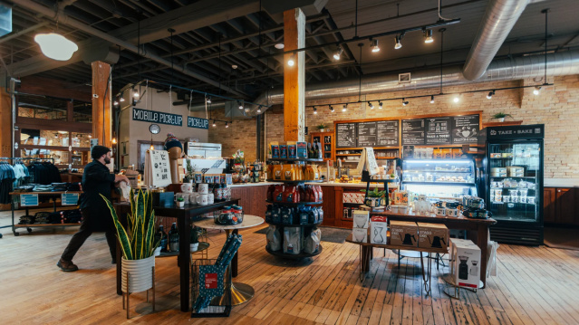 Interior of Stone Creek Coffee café featuring a warm, rustic design with wooden floors, exposed brick walls, coffee displays, refrigerated case, and barista counter.