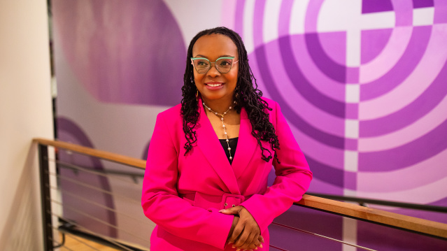 LaShawndra Vernon stands with hands clasped in front of a larger purple mural