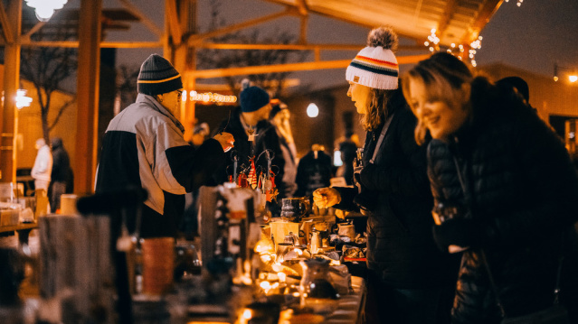 Visitors bundled in winter coats browse glowing vendor stalls at a festive outdoor holiday market in Milwaukee.