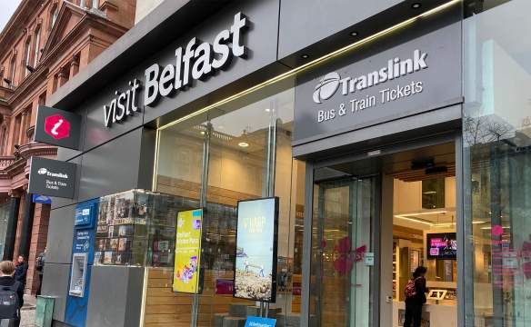An exterior of the Belfast Welcome Centre with a tourist using a touch screen inside.