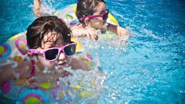 Two toddlers wearing sunglasses and floaties swim ar Edinburgh Aquatic Center.