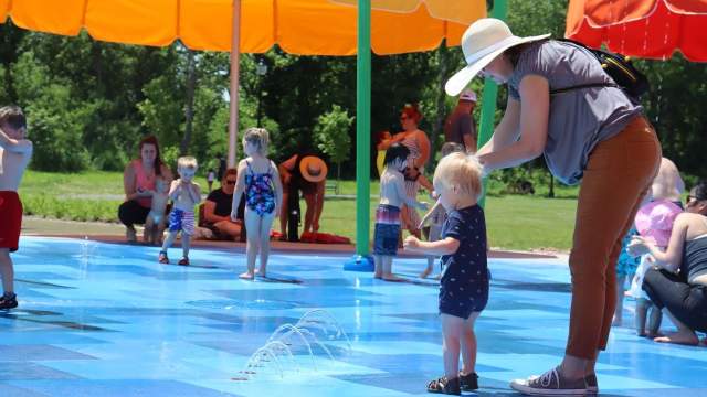 Mother leads toddler to a water sprinkler at Spray Pad at Youngs Creek Park IN Festival Country Indiana