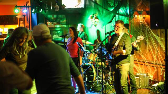 Person singing into microphone while playing guitar with a band playing late night at the Gate House on Mackinac Island.