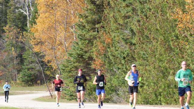 A group of runners passes by trees with gorgeous fall colors during Mackinac Island's annual Great Turtle Trail Run