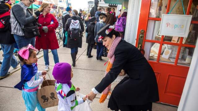 A shop owner bends down to put candy in the bags of young trick-or-treaters during Mackinac Island’s Halloween Weekend.