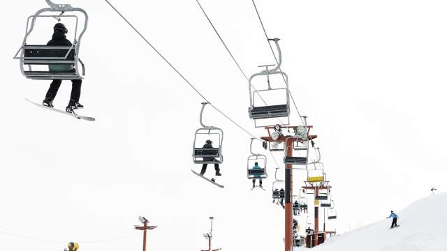 Skiers and snowboarders riding a ski lift up a snowy slope on a bright winter day.