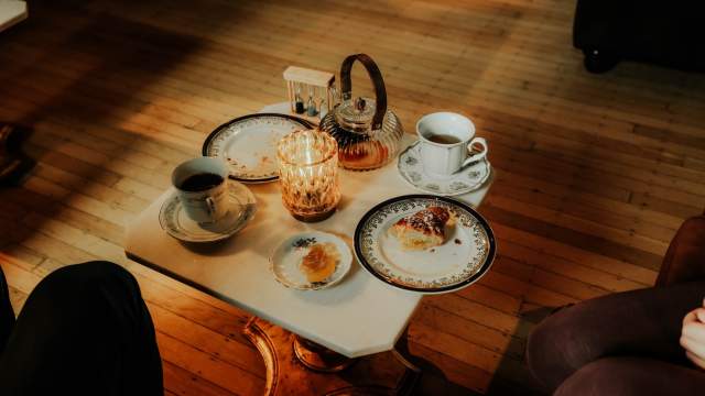 A cozy coffee table scene with two cups of coffee or tea, plates with partially eaten pastries, and a lit candle on a wooden floor.