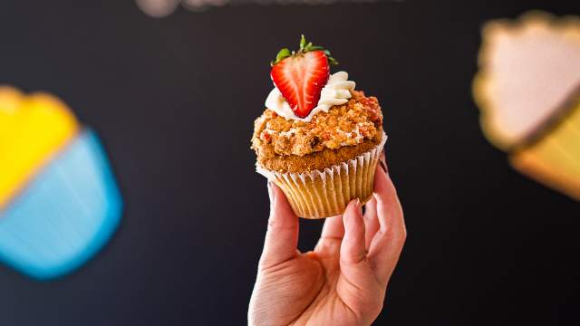 a hand holding up a cupcake with a strawberry on top