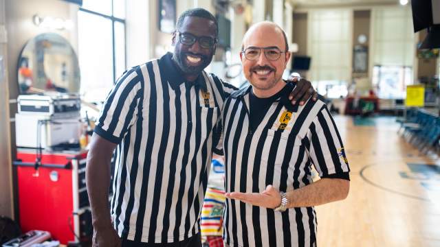 Gaulien 'Gee' Smith, a Black man with glasses and a beard, stands with his arm around David Caruso, a white man with glasses and a goatee. Both men are smiling and wearing matching black and white striped referee shirts.
