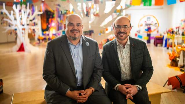 Jacobo Lovo and David Caruso sit together smiling in Latino Arts Center