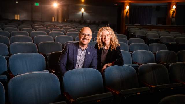 David Caruso and Susan Varella sit smiling in blue theater chairs