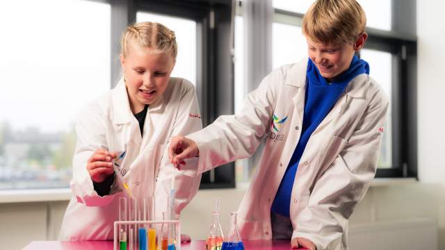 En gutt og en jente med labfrakker drypper farget væske i reagensrør