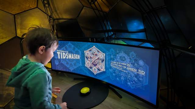 Spent gutt sitter foran skjermen i "Tidsmaskinen" på Fredrisktad museum