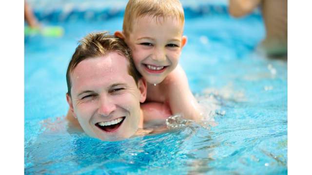 En liten gutt henger etter pappa'n når de svømmer