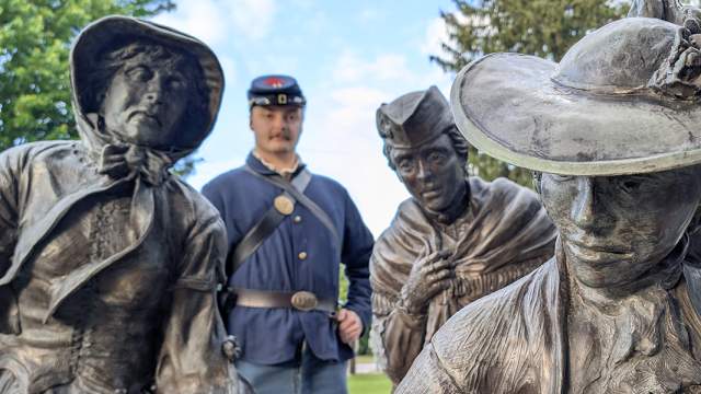 A soldier standing behind three women statues depicting women in the colonial age