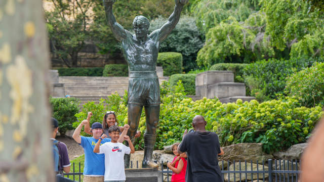 A mother and two sons posing with their arms in the air showing off their muscles in front of the Rocky Statue in Philadelphia