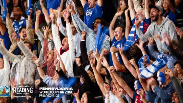 A crowd of people in stadium seats with their arms in the air cheering