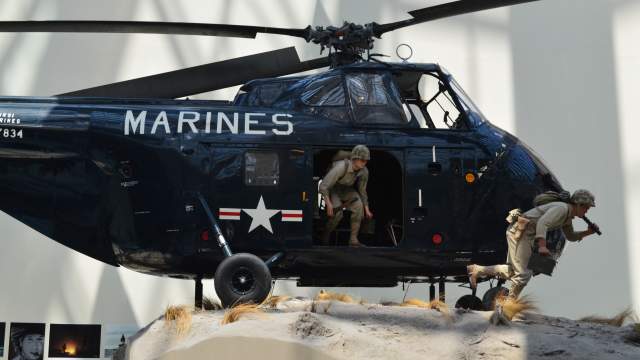 a navy helicopter with the word "marines" on the front with 2 statues of men coming out of the helicopter