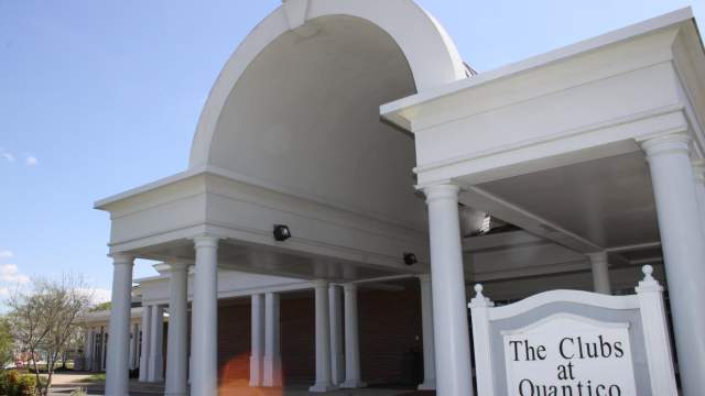 A white and brick building with a sign out front that says "The Clubs at Quantico"