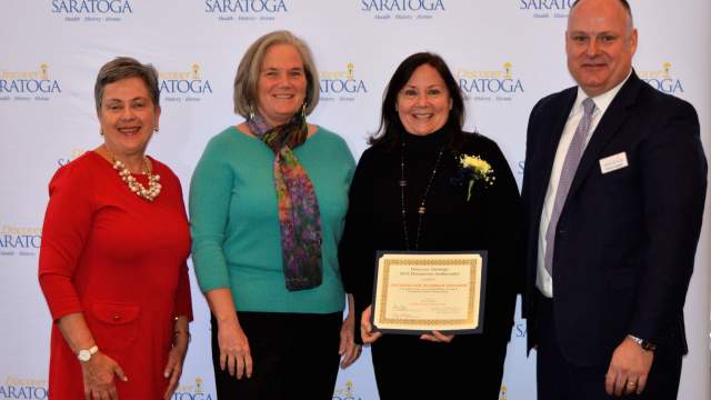 Group of four people standing in front of Discover Saratoga's step and repeat while accepting hometown ambassador award at Saratoga Springs City Center