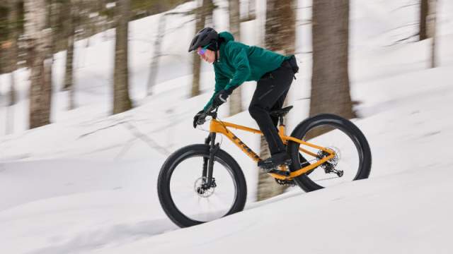 Cyclist on Fat Tires Bike cycles down a snowy mountain trail.