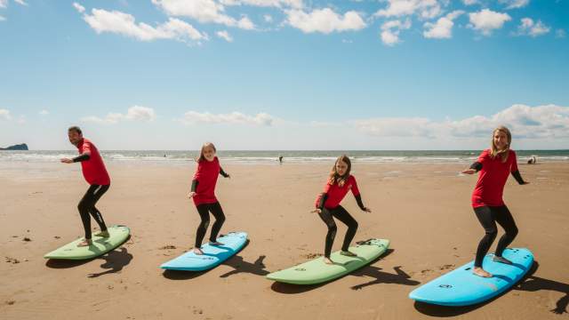 4 people standing on surf boards on a beach in Swansea Bay