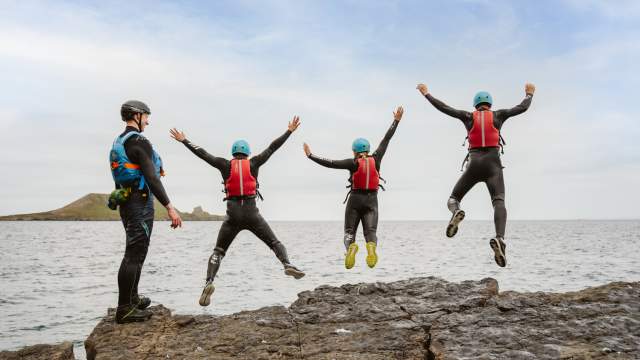 Group of people coasteering and jumping into water while instructor watches on