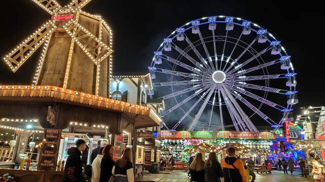 customers walking past stalls and big wheel at winter wonderland