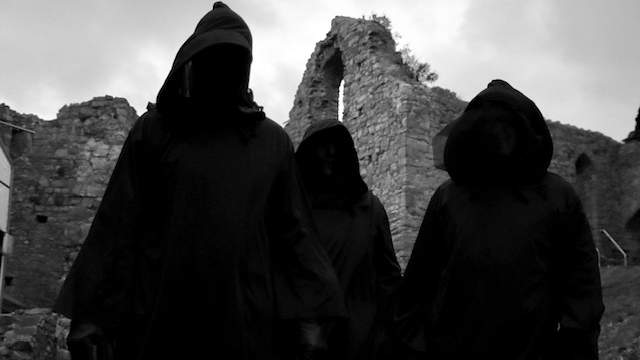 Three figures wearing hooded cloaks