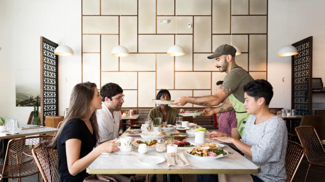 Man Serving Food To 3 People At A Table In Laziz Kitchen