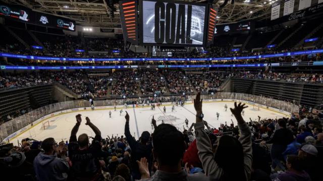 Hockey arena with fans cheering. scoreboard that reads GOAL, while players are on the ice sheet.